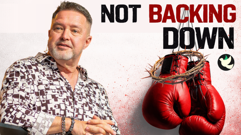 Man in a patterned shirt sits beside red boxing gloves with a crown of thorns, accompanying the 'Not Backing Down' message (motivational/promotional image).